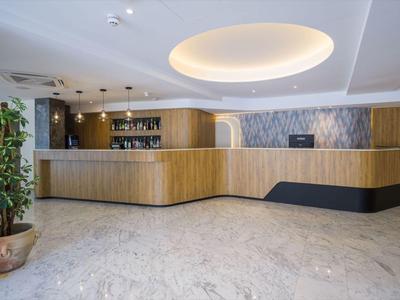 Moderner Hotel-Empfang mit hellem Marmorfußboden, hölzernem Tresen und Pflanze in Topf.