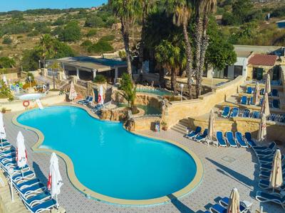Poolbereich mit blauer Liegen umgeben von Palmen und Sonnenschirmen in einer Hotelanlage.
