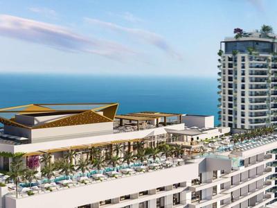 Moderner Hotelkomplex am Meer mit Pool, Liegestühlen und Hochhaus im Hintergrund.