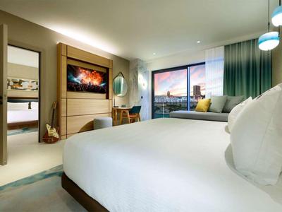Modernes Hotelzimmer mit großem Bett, Balkon und Blick auf die Stadt bei Sonnenuntergang.