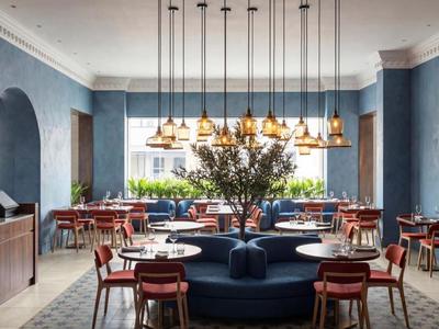 Moderner Hotel-Loungebereich mit blauen Wänden, roten Sesseln und großem Fenster.