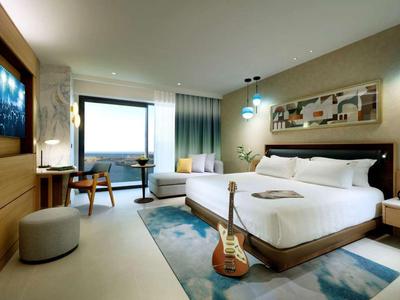 Modernes Hotelzimmer mit großem Bett, Schreibtisch, Stuhl und großer Fensterfläche.