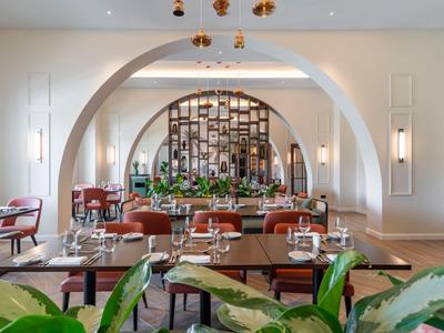 Elegant restaurant met grote bogen, koperen lampen en tafels versierd met groen.