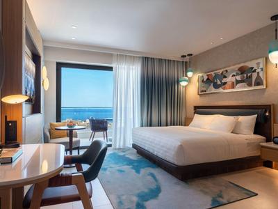 Modern hotelkamer met groot bed, bureau en uitzicht op zee.
