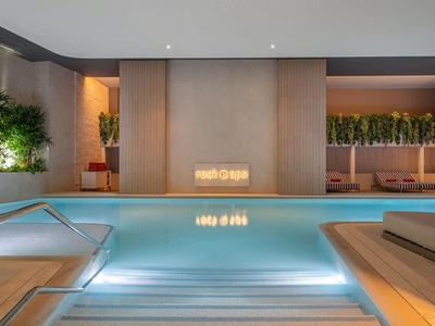 Moderne binnenzwembad met waterval, omringd door planten en rustgevende verlichting.