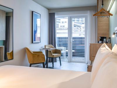 Modernes Hotelzimmer mit großem Bett, Sitzecke und Balkon mit Blick nach draußen.