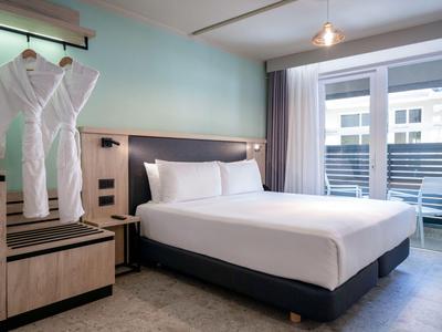 Modernes Hotelzimmer mit großem Bett, Bademänteln und Balkon mit Blick nach draußen.
