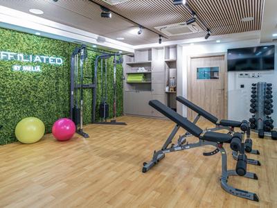 Moderner Fitnessraum mit Trainingsgeräten, Hanteln und Wand mit grünem Pflanzenmotiv.