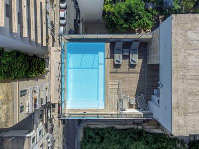 Moderner Innenhof mit blauen Schwimmbad, Liegestühlen und umgebenden Gebäuden in einer Stadt.