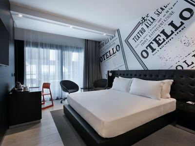 Modernes Hotelzimmer mit großem Bett, Schreibtisch, Stuhl und bodentiefen Fenstern.