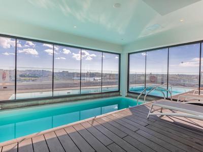 Moderner Poolbereich mit großen Glasfenstern und Aussicht auf die Stadt und das Meer.