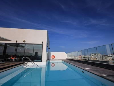 Moderner Hotelpool auf Dachterrasse mit Glasgeländer und klarem blauen Himmel.