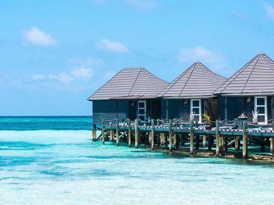 Bungalows auf Stelzen über klarem türkisblauem Wasser unter blauem Himmel.