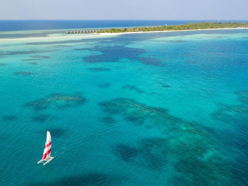 Ein Segelboot fährt über klares, türkisfarbenes Wasser nahe einer flachen Insel.
