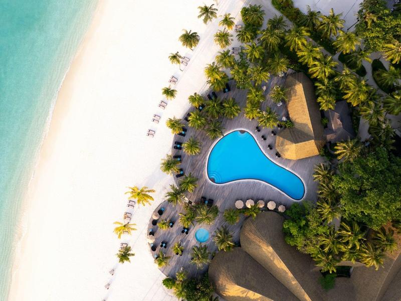 Luftaufnahme eines Hotels mit tropischem Pool neben weißem Sandstrand und Palmen.