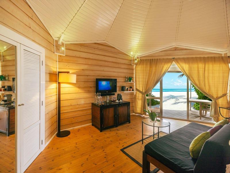 Gemütliches Hotelzimmer mit Holzwänden, TV, Sitzbereich und Blick auf den Strand.