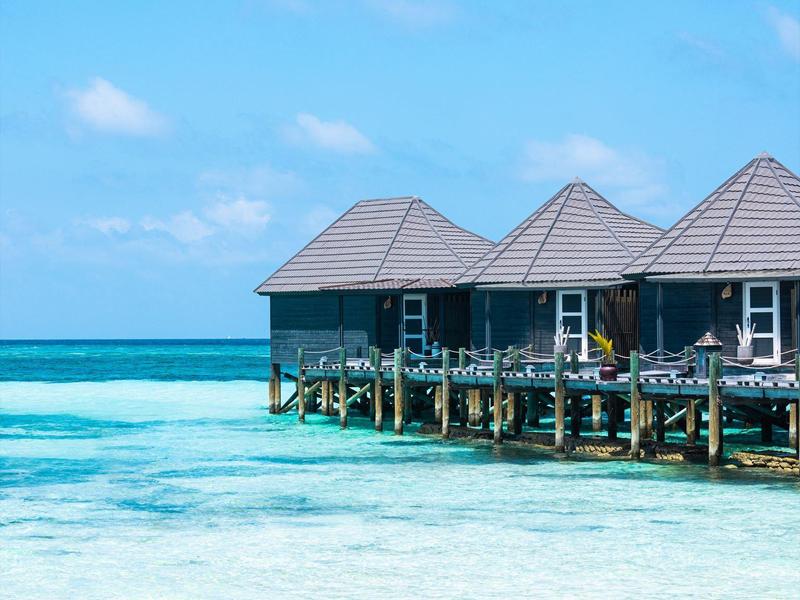 Bungalows auf Stelzen über klarem türkisblauem Wasser unter blauem Himmel.