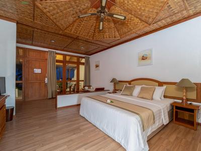 Schlafzimmer mit Holzdecke, Doppelbett, Nachttischen, Ventilator und Holzboden in warmen Farben.