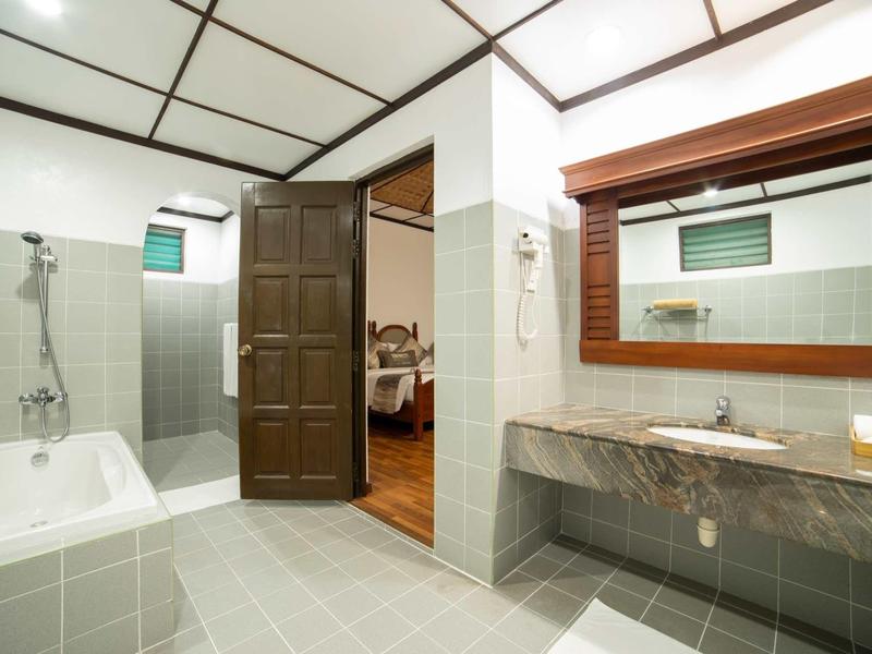 Geräumiges Badezimmer mit grauen Fliesen, Badewanne, großer Spiegel und Waschbecken aus Marmor.