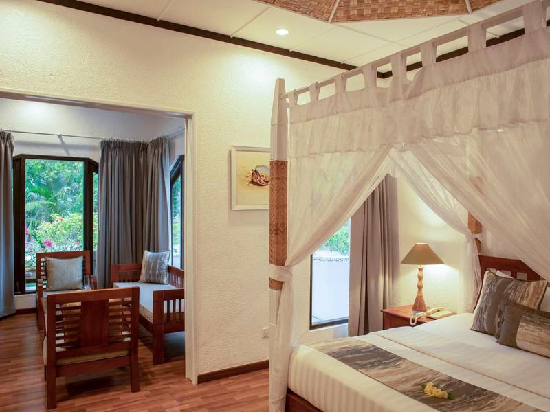 Gemütliches Schlafzimmer mit Himmelbett, angrenzendem Sitzbereich und holzfarbenem Boden.