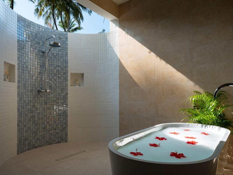 Offene Dusche mit Mosaikfliesen und freistehender Badewanne mit Rosenblättern und Pflanze.