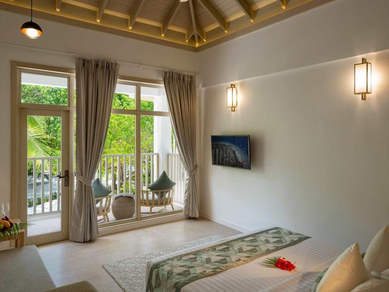 Helles Schlafzimmer mit großem Fenster, Balkon, Doppelbett, Teppich und Wand-TV in warmen Farben.