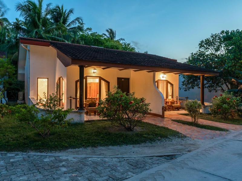 Ein einzelnes Haus mit warm beleuchteten Fenstern und offener Veranda bei Abenddämmerung.