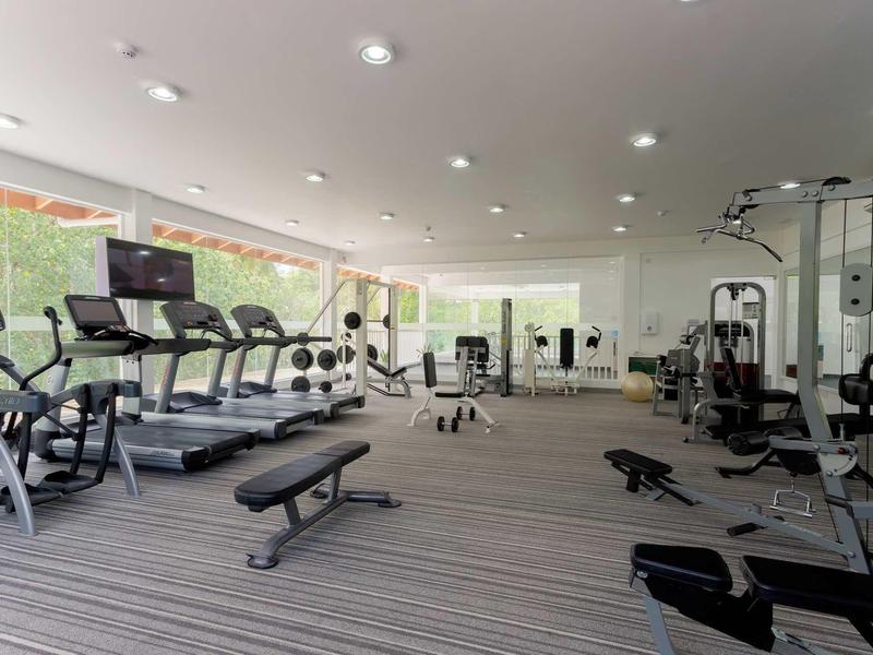 Heller moderner Fitnessraum mit Laufbändern, Hanteln, Kraftgeräten und großem Fensterfront.