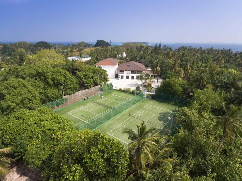 Haus mit rotem Dach umgeben von dichter grüner Vegetation und einem Tennisplatz im Garten.