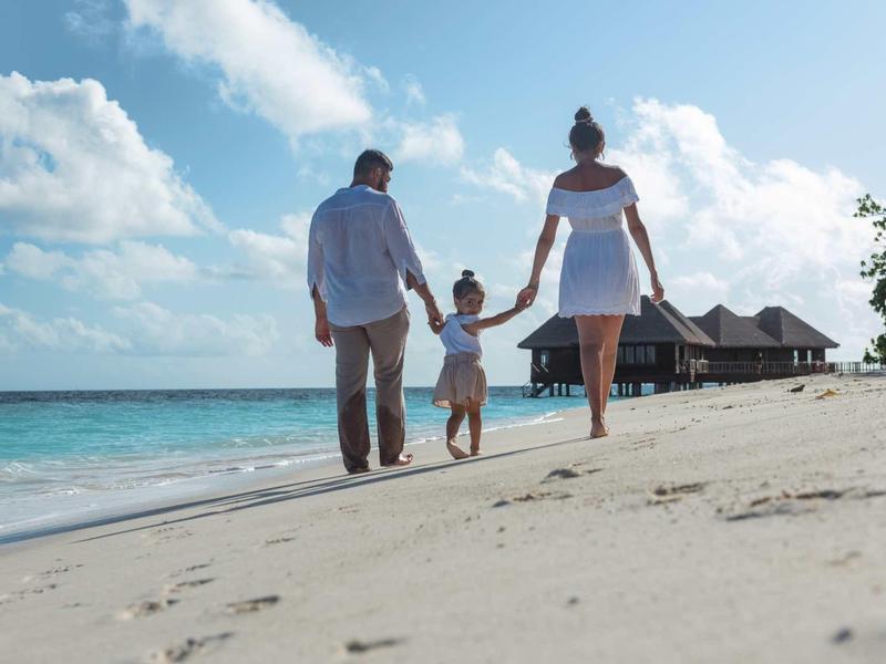 Familie mit kleinem Kind hält Hände und läuft barfuß am Sandstrand am Meer.