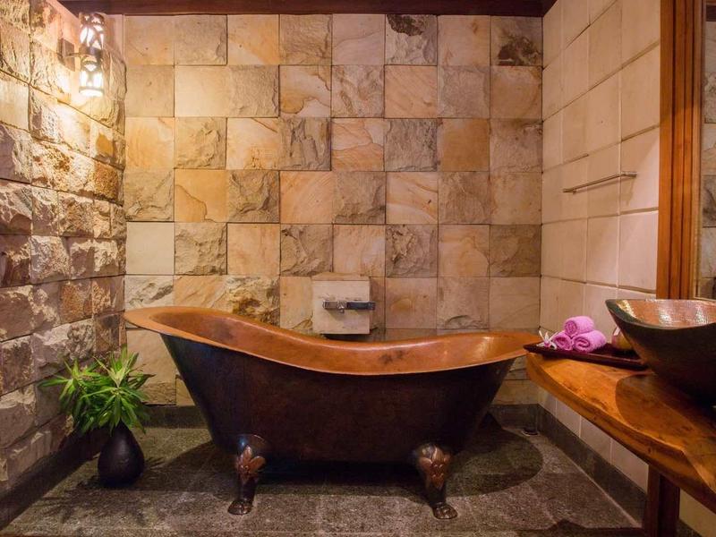 Helles Bad mit freistehender Holzwanne, Steinwänden und holzvertäfelter Decke.