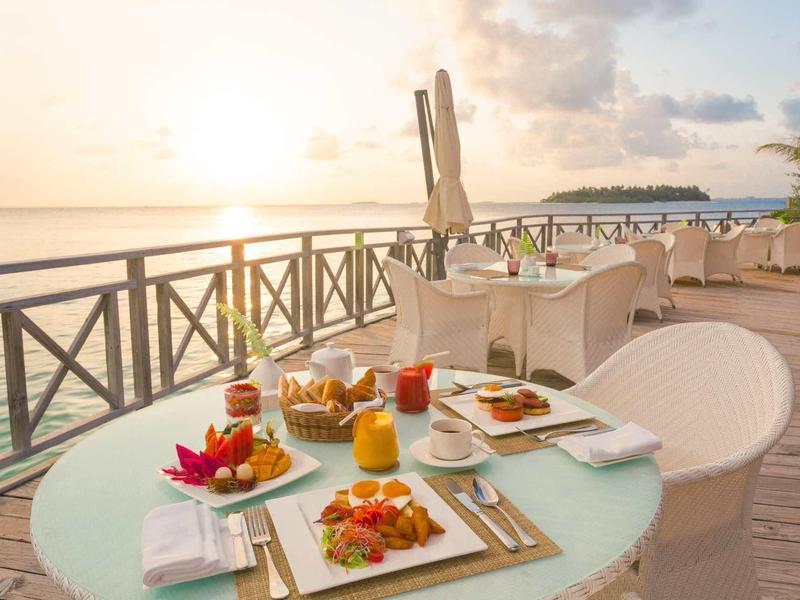 Terrassentisch mit Frühstück, Meerblick, Sonnenuntergang, gedeckte Tische und Holzgeländer.