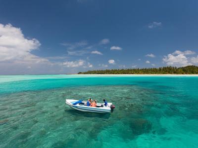 Kleines Boot mit Personen auf klarem, türkisfarbenem Wasser nahe einer bewaldeten Insel.