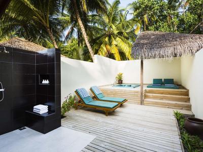 Outdoor-Duschbereich neben zwei Liegestühlen und einem überdachten Sitzbereich mit Palmen im Hintergrund.