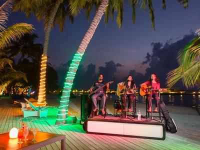 Band spielt abends auf einer beleuchteten Terrasse am Wasser mit Palmen.