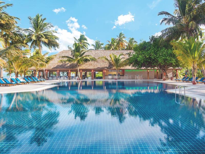 Großer Pool umgeben von Liegestühlen und Palmen bei sonnigem Himmel