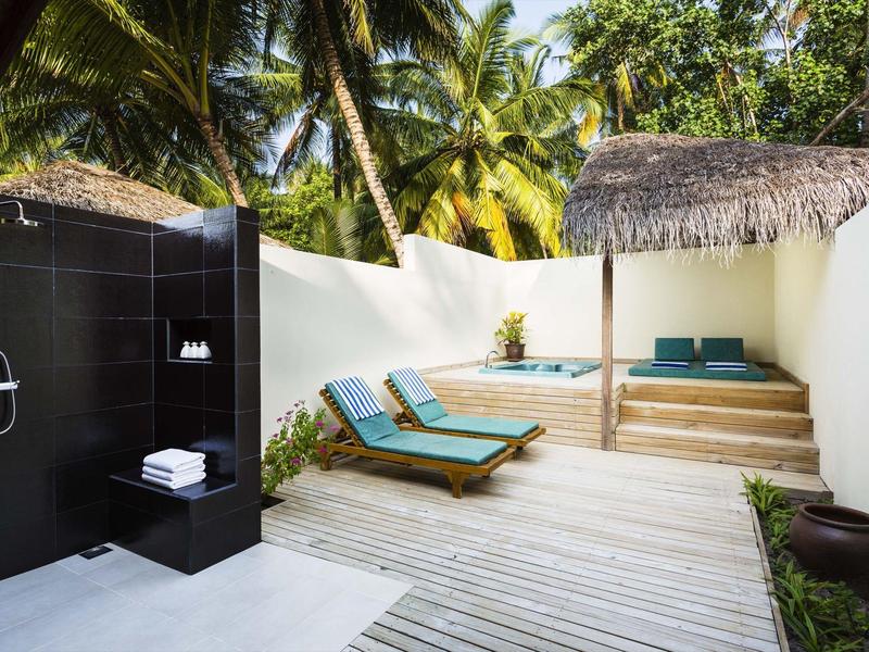 Outdoor-Duschbereich neben zwei Liegestühlen und einem überdachten Sitzbereich mit Palmen im Hintergrund.
