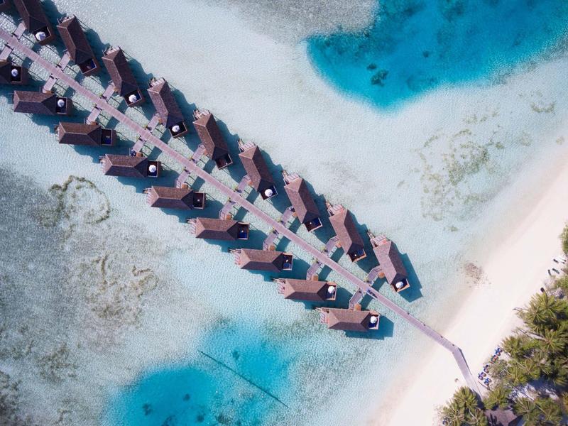 Vogelperspektive einer Strandbar mit Liegestühlen im klaren blauen Wasser und weißem Sandstrand.