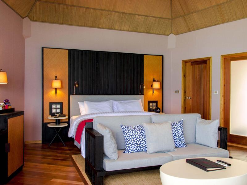 Modern eingerichtetes Hotelzimmer mit Bett, Sofa und Holzboden in warmen Tönen.