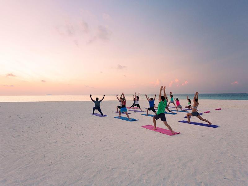 Gruppe macht Yoga am Strand bei Sonnenaufgang mit entspannter Stimmung.