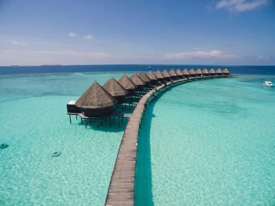Reihenförmige Holzbungalows auf Pfählen über klarem, türkisfarbenem Wasser unter blauem Himmel.