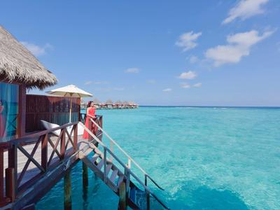 Bungalow auf Pfählen über klarem türkisfarbenem Wasser unter blauem Himmel mit weißen Wolken.