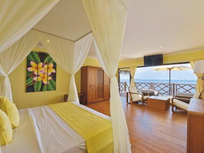 Schlafzimmer mit Himmelbett, gelber Dekoration, Holzfußboden und Meerblick durch große Fenster.