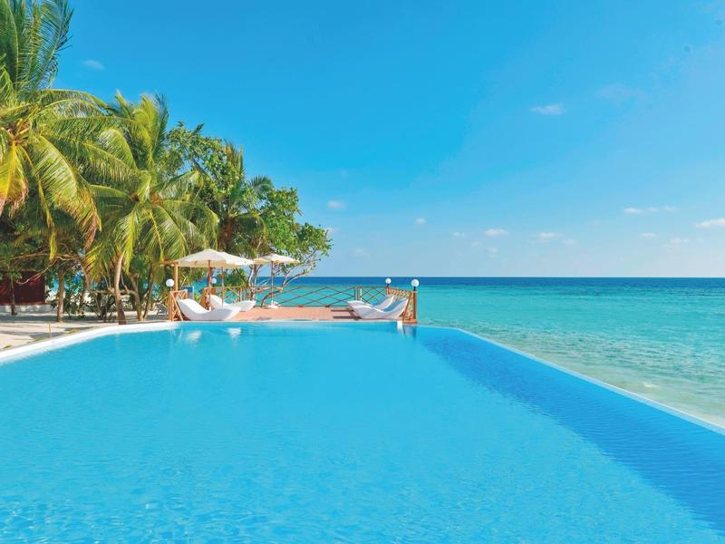 Infinity-Pool mit Blick auf das Meer und Palmen unter blauem Himmel.