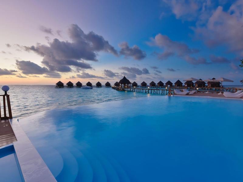 Infinity-Pool mit Blick auf das Meer und Bungalows bei Sonnenuntergang