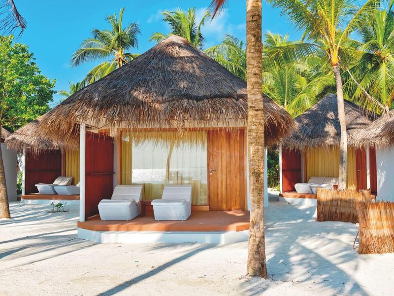 Strandbungalow mit Strohdach und Liegestühlen umgeben von Palmen auf weißem Sand