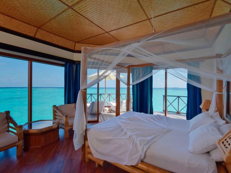 Hotelzimmer mit Himmelbett und Meerblick durch große Fenster und Balkon.