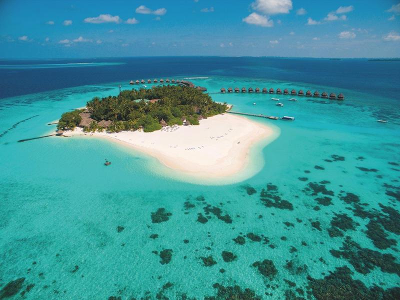 Kleine tropische Insel mit weißem Sandstrand und über Wasser gebauten Bungalows im klaren blauen Meer.