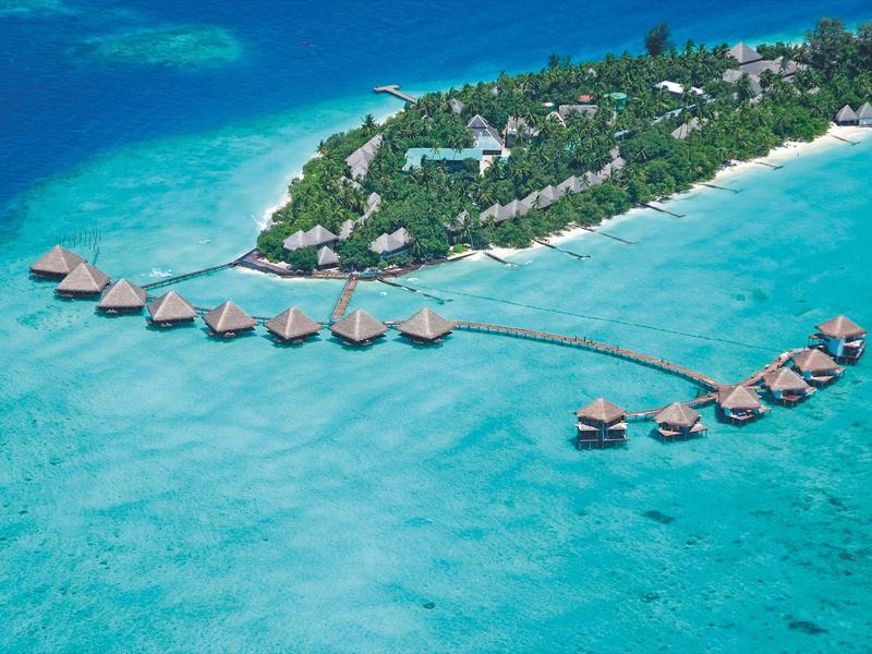 Tropische Insel mit grünem Wald, umliegenden weißen Stränden und über Wasser gebauten Bungalows.