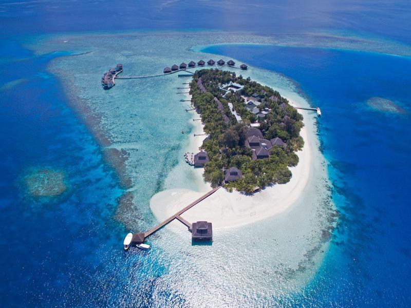 Kleine tropische Insel mit weißem Sand, üppiger grüner Vegetation und Steg im klaren blauen Meer.